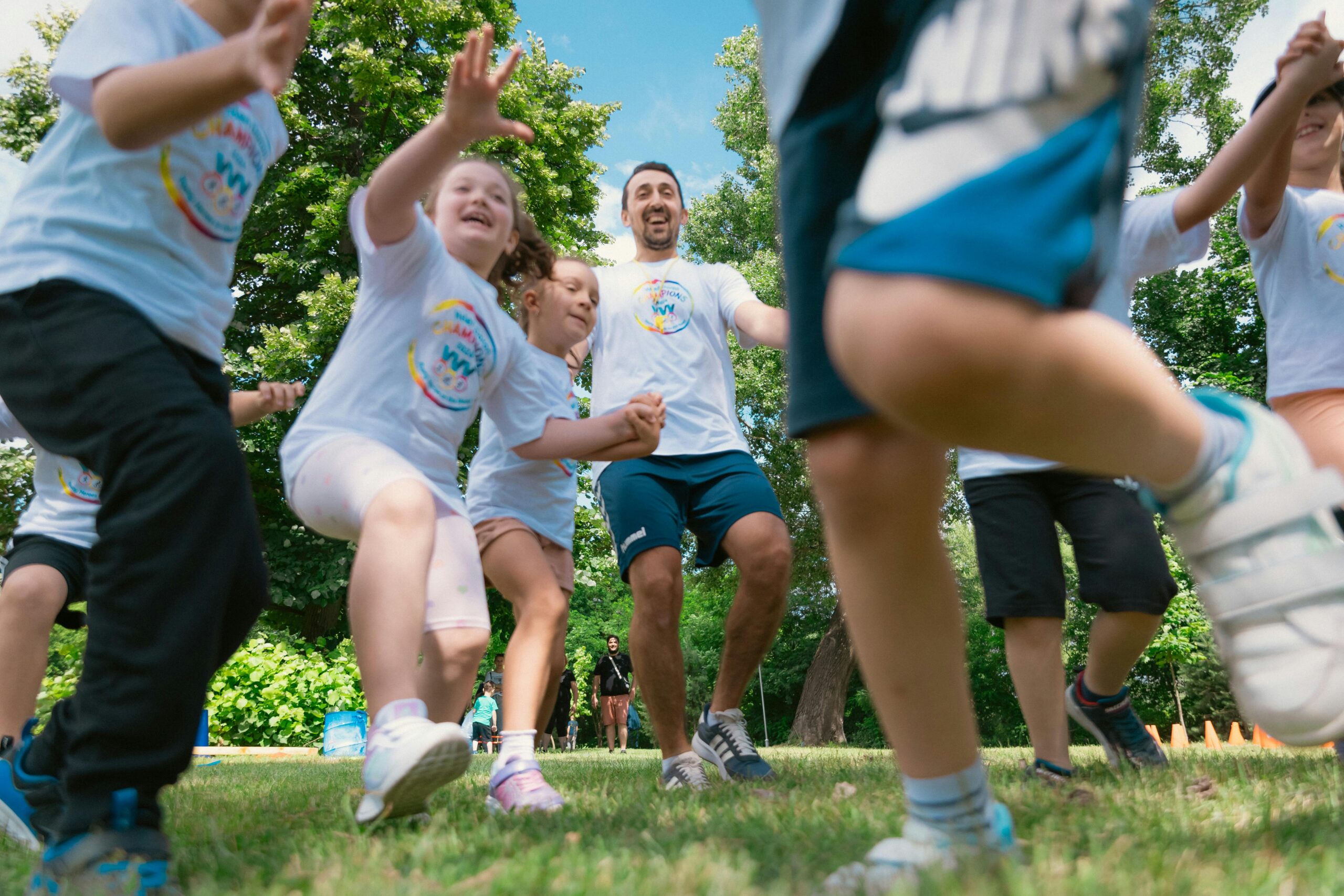 Joyful group of children and adult engaging in playful activities in a sunny park setting.