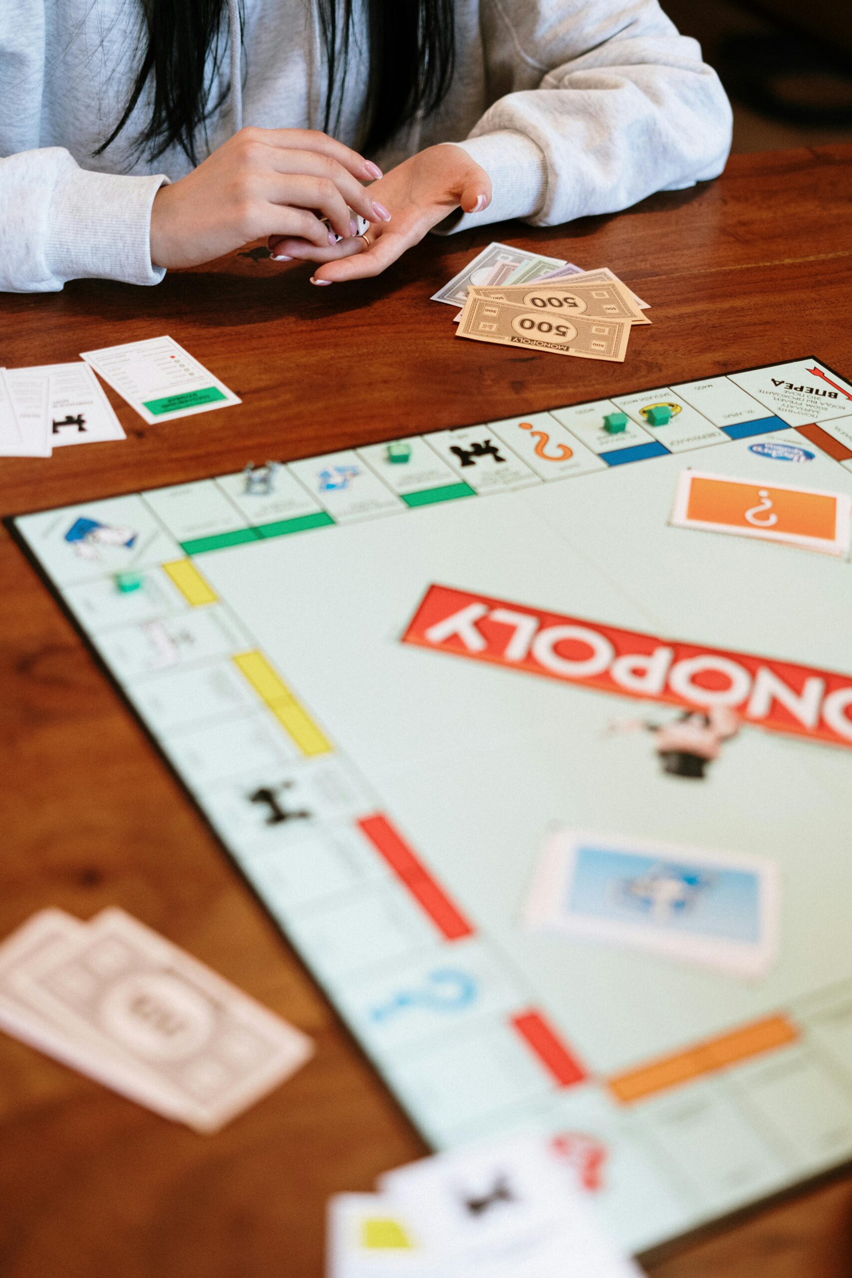 Close-up of people playing Monopoly, showcasing board and game pieces on a wooden table.